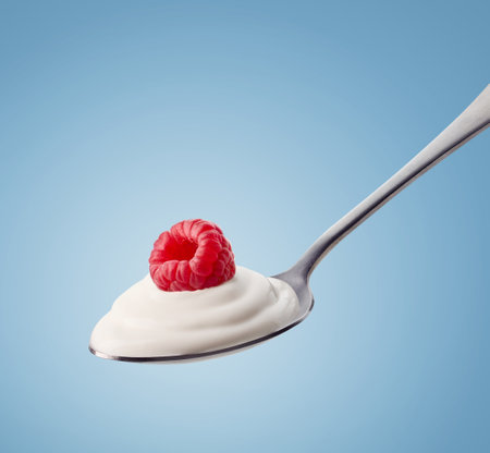 Spoon of fresh natural greek yogurt and raspberry on blue backgroundの写真素材