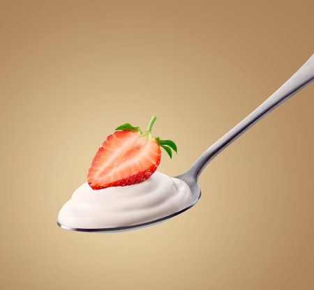 Silver spoon of fresh greek yogurt and strawberry on light brown backgroundの写真素材