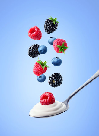 Silver spoon of fresh greek yogurt and falling wild berries on blue background. Raspberry, blueberry and blackberryの写真素材