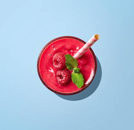 Glass of red raspberry smoothie on blue background, top viewの写真素材