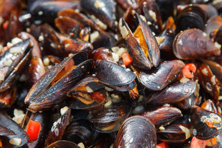 Mussels cooked in sauce with vegetables in a frying pan.
