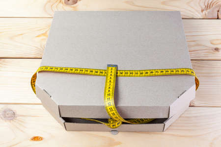 Yellow rag tape measure and pizza box. The concept of proper nutrition and weight loss.の写真素材