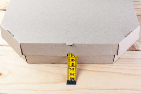 Yellow rag tape measure and pizza box. The concept of proper nutrition and weight loss.の写真素材