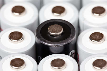 AA batteries are located close to each other. Close-up of all white batteries, except one black, on a white background. Battery technology.の写真素材