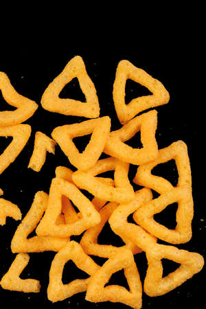 Cheese puff sticks, crunchy corn snack, unhealthy food. Snack triangle isolated over black...
