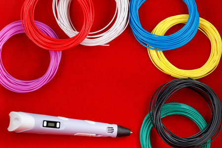 3d pen, and kit of colorful PLA or ABS plastic filament on red background. close up