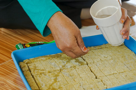 A person is preparing homemade snacks by pouring liquid onto a tray filled with sliced ingredients....