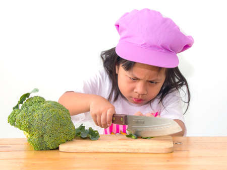 Little girl is cutting vegetable for salad using kitchen knifeの写真素材