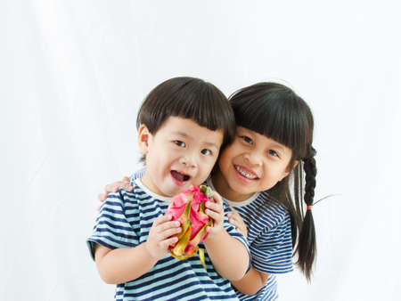 Little boy holding dragon fruit in hand and beautiful girl stand up smiling on white background,...