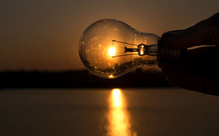 Finger holding light bulb on sunset background, image silhoutte background,