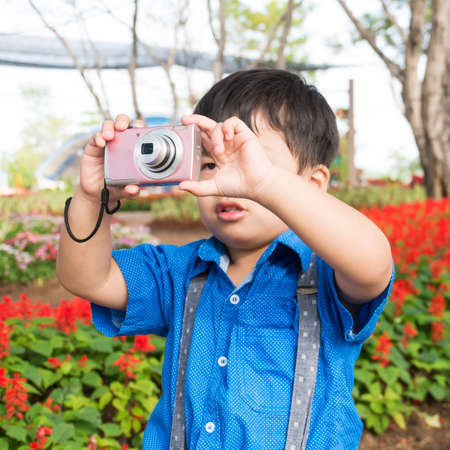 Little asian boy take camera on garden flower,の写真素材