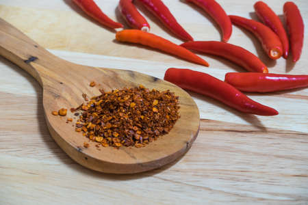 Cayenne pepper on wooden ladle and on raw chilli background,