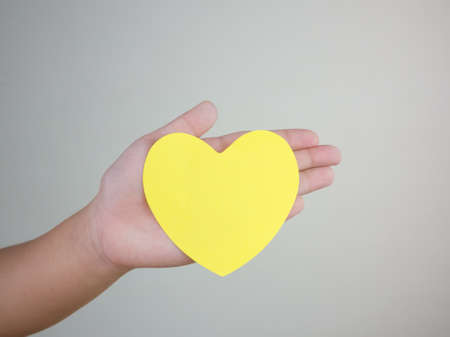 heart paper in hand on wall background, yellow color heart in hand,