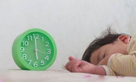 alarm clock with little boy sleeping on bed, green alarm clock,の写真素材