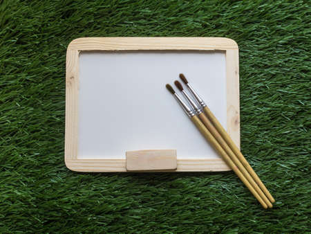 White board and paintbrush on green grass background,