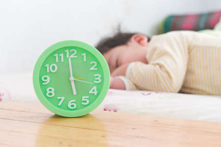 alarm clock with little boy sleeping on bed, green alarm clock, wooden table,