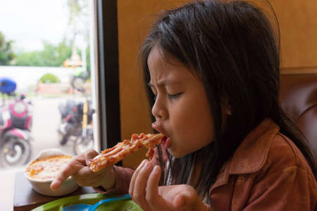 Asian Little girl eating pizza in restaurantの写真素材