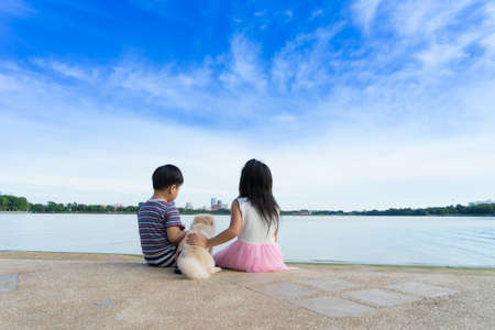 Little Boy and cute girl sitting by the water with dog on blue sky background,の写真素材