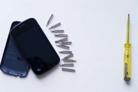 Broken phone and screwdriver placed on wooden table.の写真素材