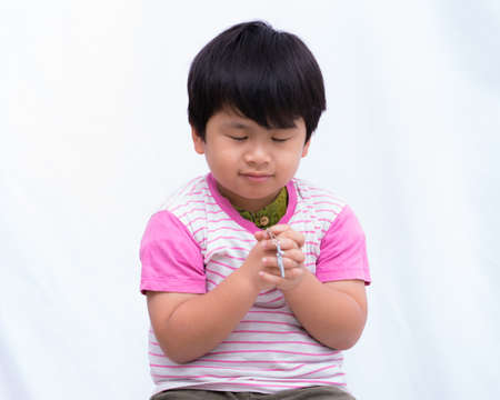 Defocused crucifix in hand cute boy with close one's eyes on white background,の写真素材
