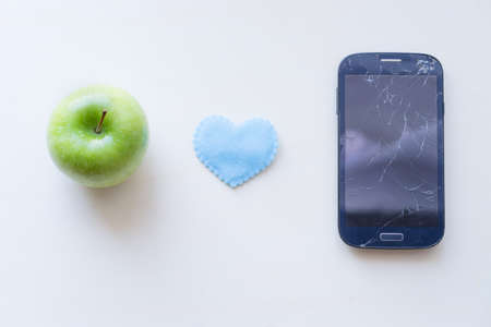 Cell Phone Screen Cracks and blue heart with green apple fruit on white wooden background,の写真素材