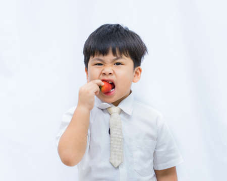 Portrait cute Asian boy eating red strawberry on white background,の写真素材
