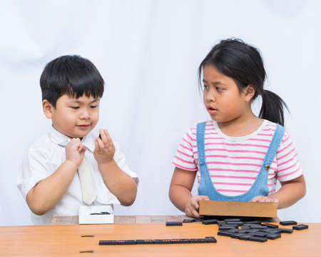 Little boy and beautiful girl playing domeno in wooden table on white background,の写真素材