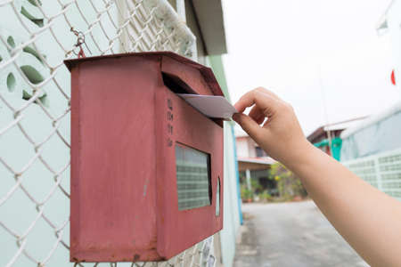 posting a letter to red british postbox on street, Closeup on a woman's hand as she is posting a letter,の写真素材