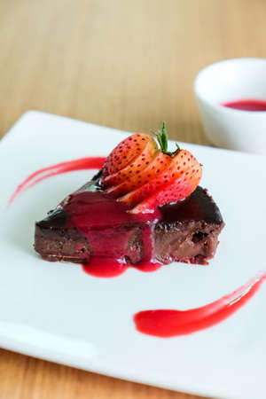 Chocolate Cake topping with sliced strawberry and raspberry sauce placed  on white square dishの写真素材