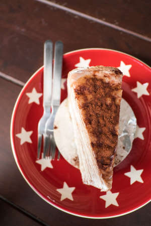 Crepe cake toped with cocoa served on red dish with white star on wooden table