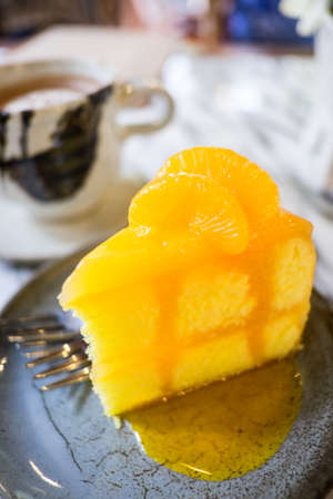 Orange cake placed on deep blue colour clay plate with small silver colour fork near a clay mug filled with hot coffee, both of them placed on marble top tableの写真素材