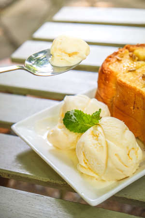 Honey toast with vanilla icecream on white square plate placed on wooden tableの写真素材