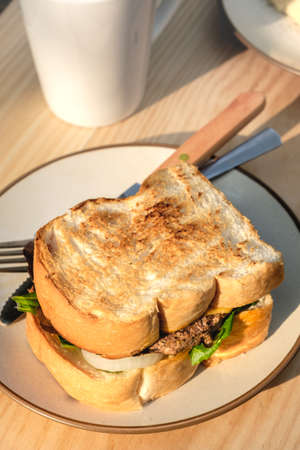 Yummy Beef and cheese Grilled Sandwich on round cream color plate with fork and knife place beside a...