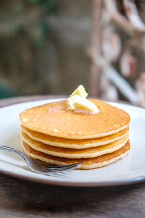 Stacked Pancake topped with butter placed on white plate on wooden tableの写真素材