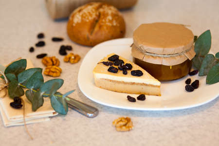 Sweet apricot jam in the glass jar and piece of tasty cake with raisins are on the plate. Knife,...