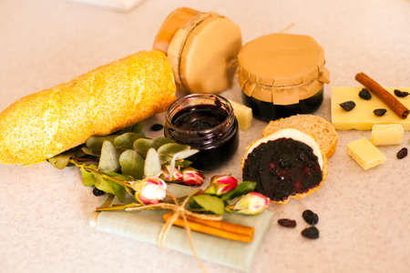 Top view of opened jar with sweet blackcurrant jam, slices of fresh bread, beautiful roses, two little jars with delicious fruit jam and white chocolate with cinnamon and raisinsの写真素材