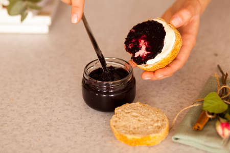 Woman's hands are spreading slice of fresh bread with sweet blackcurrant jam for breakfast