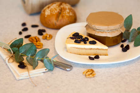 Sweet apricot jam in the glass jar and piece of tasty cake with raisins are on the plate. Knife,...