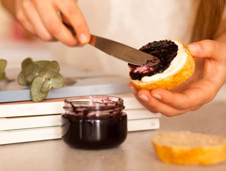 Woman's hands are spreading slice of fresh bread with sweet blackcurrant jam for breakfastの写真素材