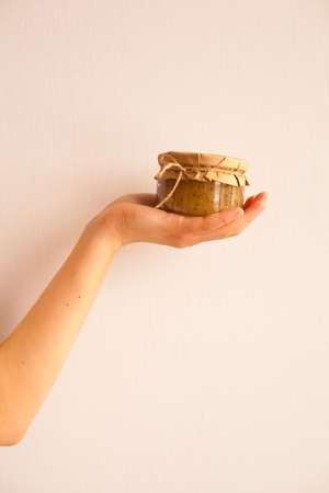 Woman's hand is holding  little glass jar with sweet banana jam on the white backgroundの写真素材