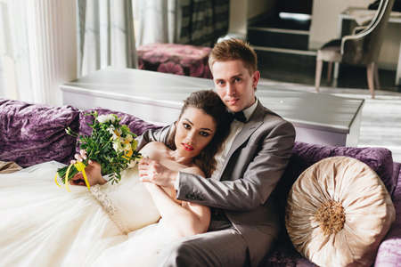 Charming newlyweds hugging and lying on the purple sofaの写真素材