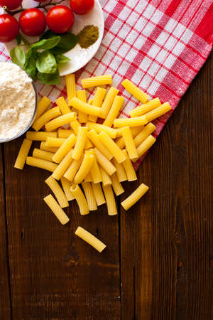 Raw pasta with fresh red cherry tomatoes on the plate near bowl of flour are on the old wooden tableの写真素材