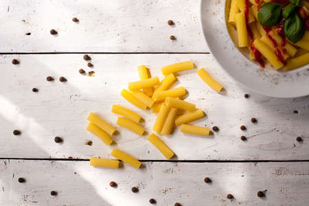 Prepared flavour pasta dish with sauce on the white plate. Raw macaroni and whole papper on the...