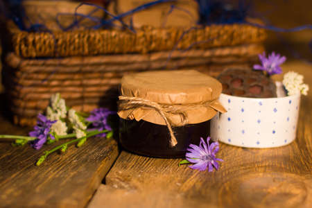 Little glass jar of sweet blackcurrant jam with cup and flowers near it. Braiding basket with jars of jam on the backgroundの写真素材