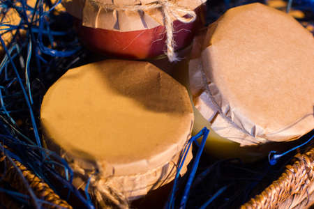 Tree glass jars of orange, blackcurrant jam and lemon kurd are in the braiding basketの写真素材