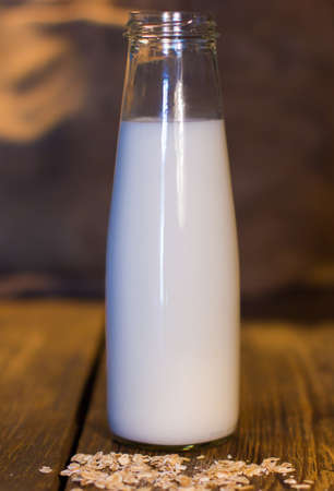 Opened glass bottle of fresh milk and oat flakes are on the wooden tableの写真素材