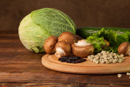 Mushrooms, cabbage, salad and grains are on the round plank on the wood tableの写真素材