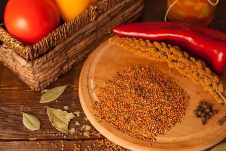 Grains and chili are on the round plank near a basket with tomatos on the wood tableの写真素材
