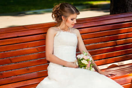 Happy bride sitting on wooden old-fashioned benchの写真素材