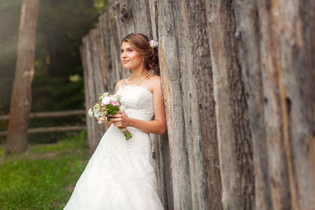 Bride in elegant wedding dress in front of wooden fenceの写真素材
